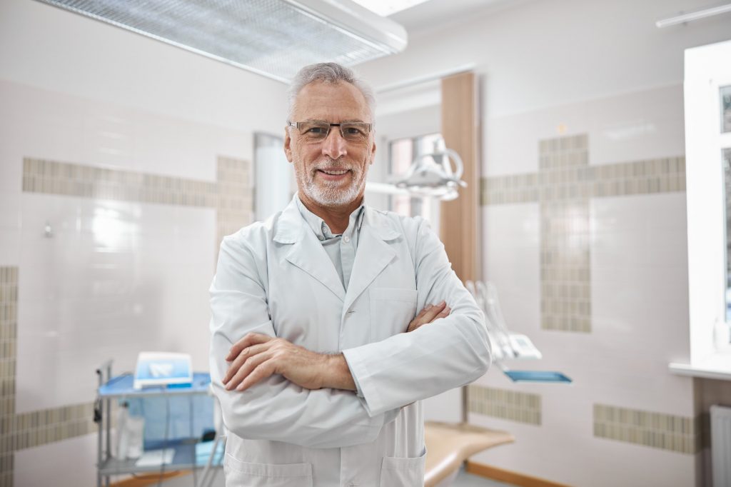 Joyful doctor standing cross-armed in dentists office